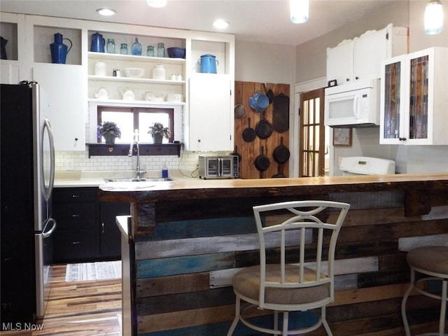 kitchen featuring freestanding refrigerator, white cabinets, a sink, and white microwave