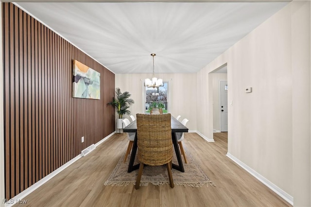 dining space featuring wooden walls, light hardwood / wood-style floors, and a notable chandelier