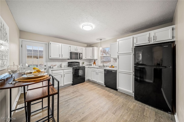 kitchen featuring pendant lighting, sink, white cabinetry, black appliances, and light hardwood / wood-style floors