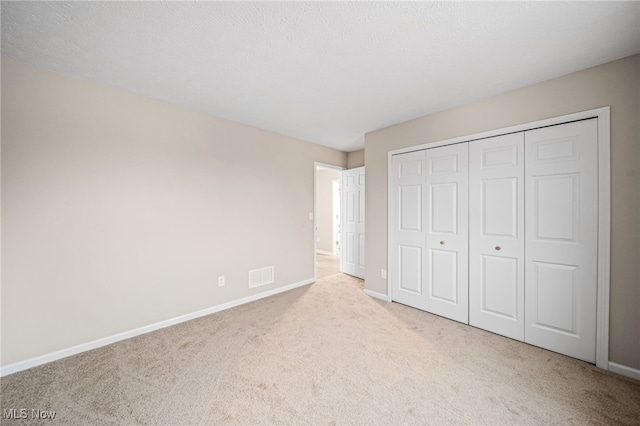 unfurnished bedroom with light carpet, a textured ceiling, and a closet