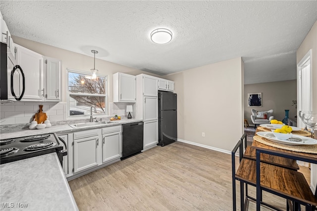 kitchen with white cabinetry, sink, hanging light fixtures, black appliances, and light hardwood / wood-style flooring