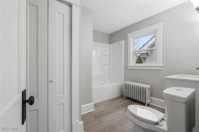 full bathroom featuring radiator, hardwood / wood-style floors, a textured ceiling, shower / washtub combination, and toilet