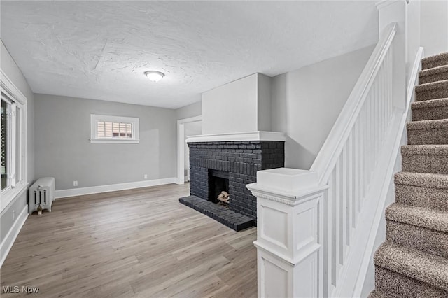 living room featuring radiator, light hardwood / wood-style floors, a brick fireplace, and a textured ceiling