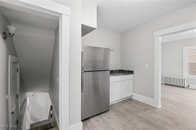 kitchen featuring radiator heating unit, white cabinetry, dark stone countertops, stainless steel fridge, and light hardwood / wood-style flooring