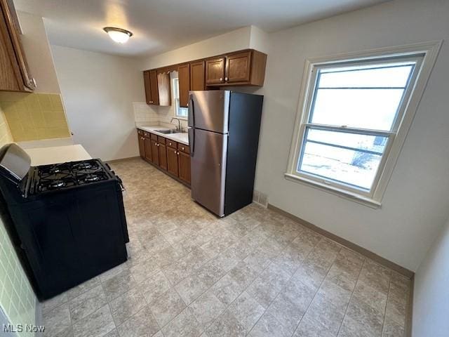 kitchen with sink, backsplash, range with gas stovetop, and stainless steel refrigerator