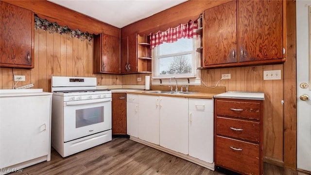 kitchen with white range with gas cooktop, sink, wood-type flooring, and wood walls