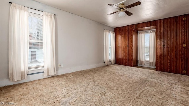 empty room featuring ceiling fan, carpet flooring, and wooden walls