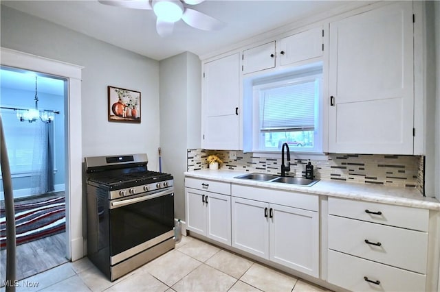 kitchen featuring sink, stainless steel gas range, tasteful backsplash, white cabinets, and ceiling fan with notable chandelier