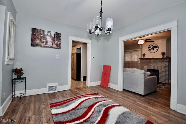 living room with ceiling fan with notable chandelier, hardwood / wood-style floors, and a brick fireplace