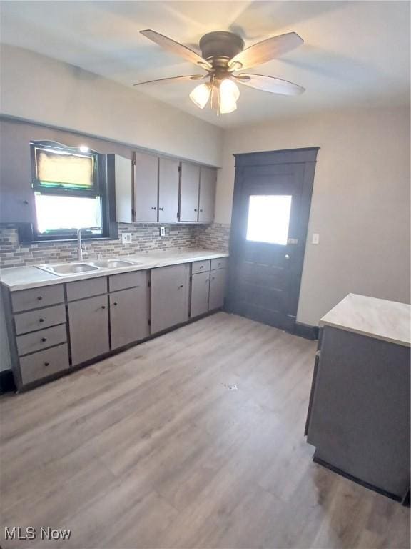 kitchen featuring sink, light hardwood / wood-style flooring, gray cabinets, ceiling fan, and tasteful backsplash