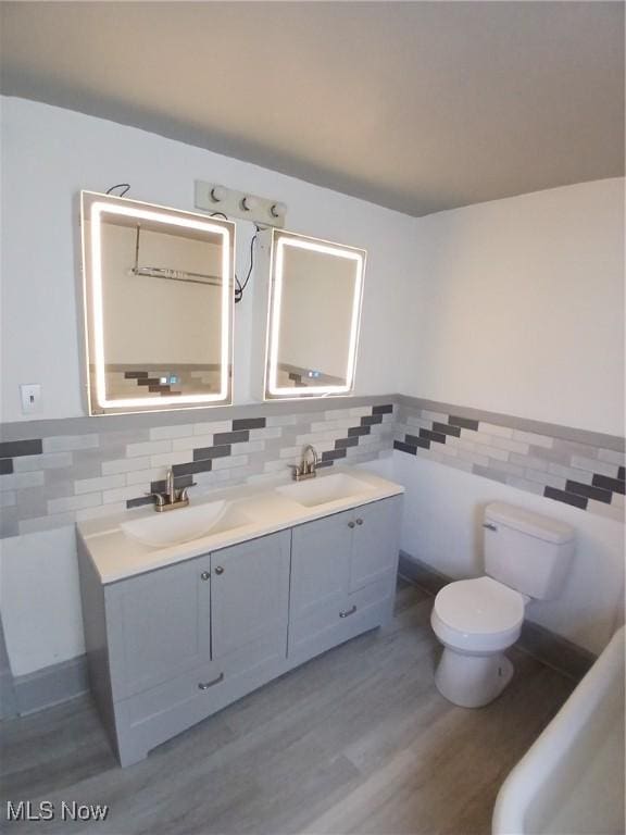 bathroom featuring vanity, hardwood / wood-style floors, toilet, and tile walls