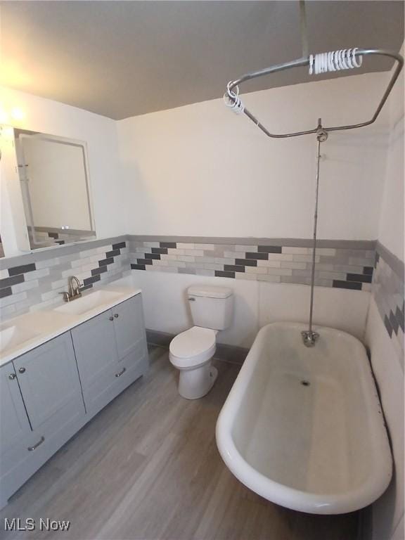 bathroom featuring tile walls, vanity, wood-type flooring, a tub to relax in, and toilet