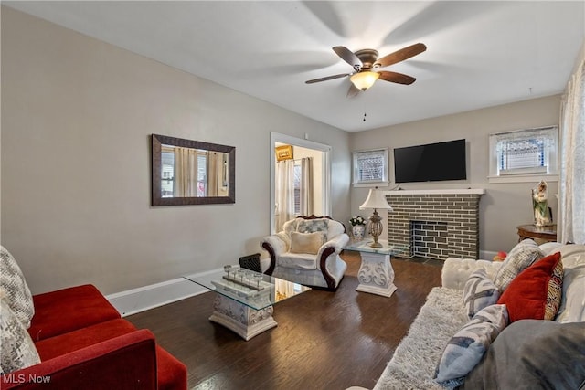 living room with a brick fireplace, dark wood-type flooring, and ceiling fan