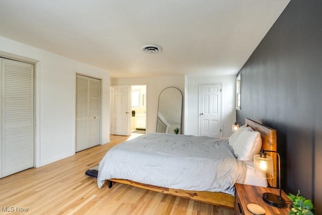 bedroom with baseboards, light wood-style flooring, visible vents, and multiple closets