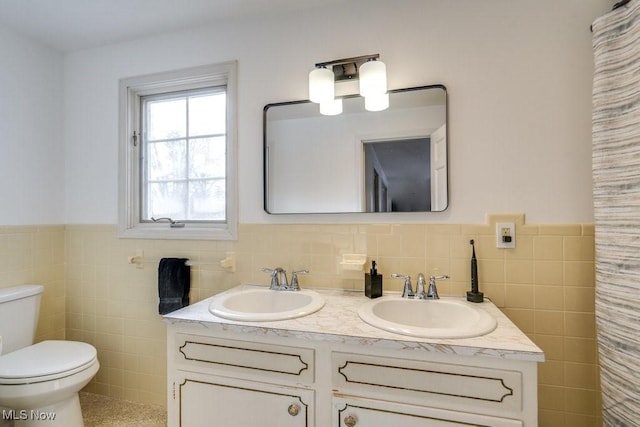 full bathroom with toilet, a wainscoted wall, tile walls, and a sink