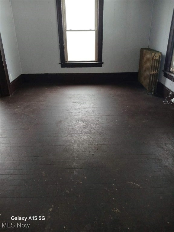 empty room with dark wood-type flooring and radiator heating unit