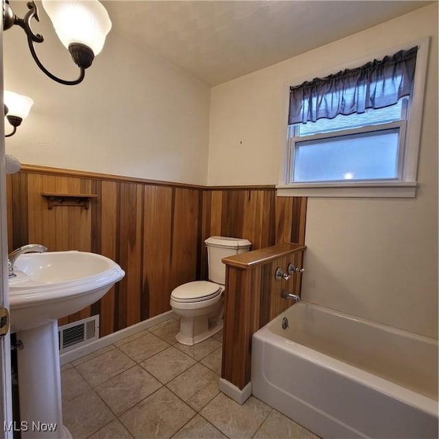 bathroom featuring tile patterned floors, a tub to relax in, toilet, and wood walls