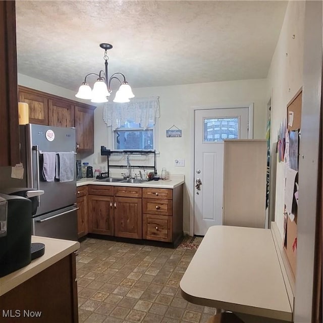 kitchen with hanging light fixtures, sink, an inviting chandelier, and stainless steel refrigerator