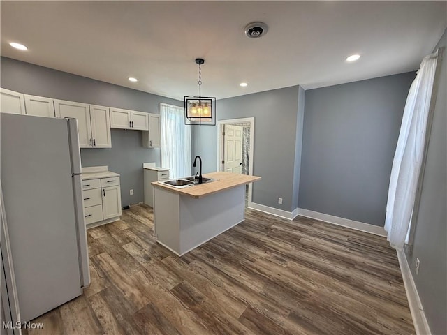 kitchen with pendant lighting, sink, fridge, white cabinets, and a center island with sink