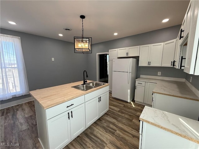 kitchen featuring sink, hanging light fixtures, a center island with sink, white refrigerator, and white cabinets