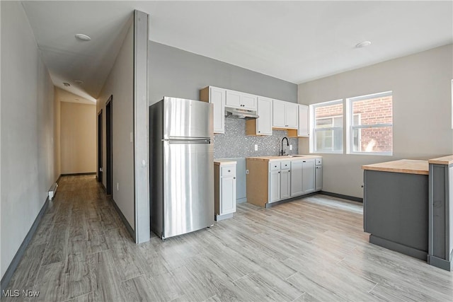 kitchen with tasteful backsplash, butcher block counters, sink, stainless steel fridge, and light hardwood / wood-style floors