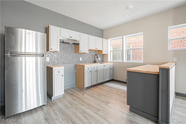 kitchen featuring white cabinetry, wooden counters, light hardwood / wood-style flooring, stainless steel refrigerator, and decorative backsplash