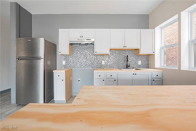 kitchen featuring sink, stainless steel fridge, light hardwood / wood-style flooring, white cabinetry, and tasteful backsplash