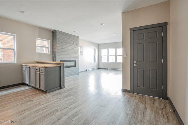 kitchen with a baseboard radiator, light hardwood / wood-style floors, and a large fireplace