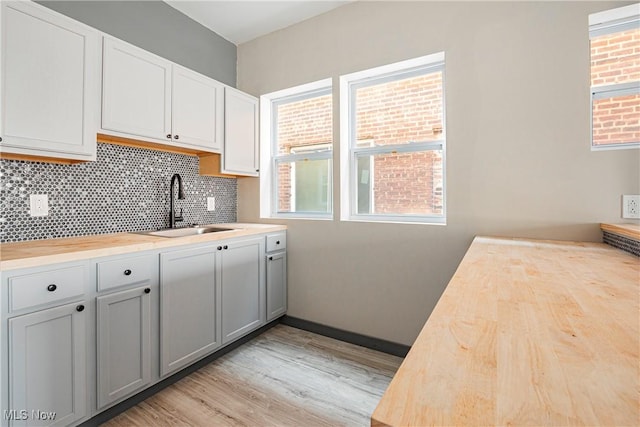 kitchen featuring sink, gray cabinets, light hardwood / wood-style flooring, butcher block counters, and tasteful backsplash