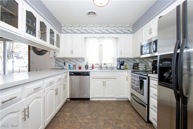 kitchen featuring backsplash, glass insert cabinets, light countertops, appliances with stainless steel finishes, and a sink