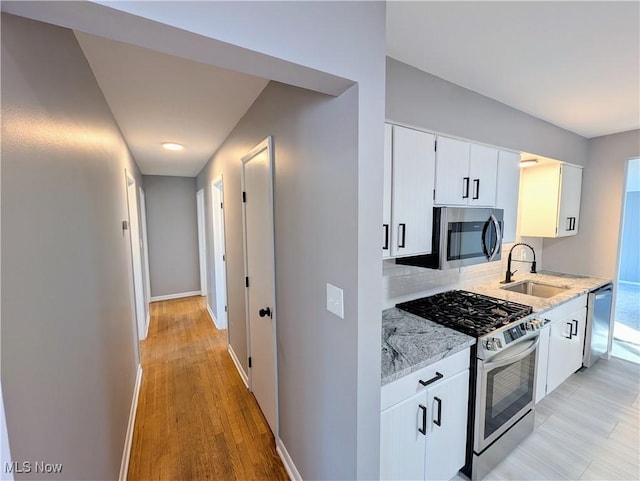 kitchen featuring sink, appliances with stainless steel finishes, light stone counters, white cabinets, and decorative backsplash