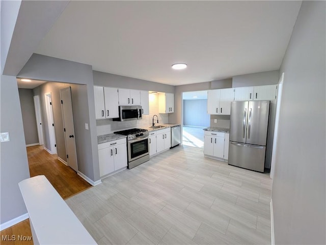 kitchen featuring sink, white cabinetry, backsplash, stainless steel appliances, and light stone counters