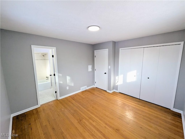 unfurnished bedroom with a closet, connected bathroom, and light hardwood / wood-style flooring