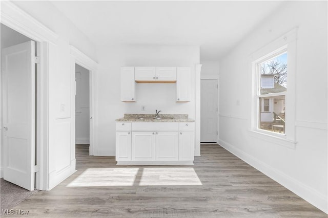 kitchen with light stone counters, sink, light hardwood / wood-style flooring, and white cabinets