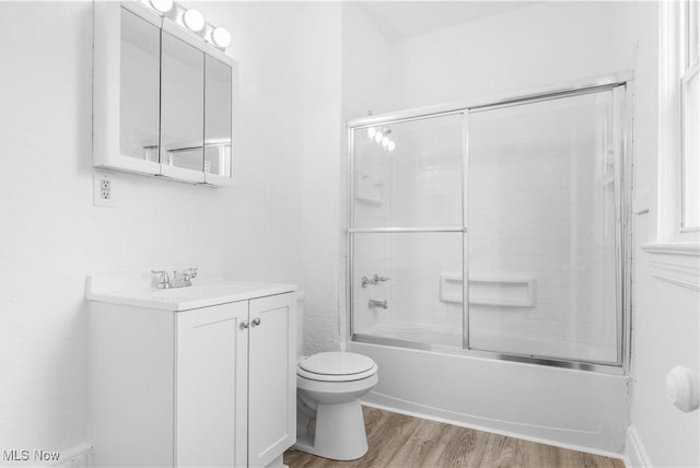 full bathroom with hardwood / wood-style flooring, vanity, shower / bath combination with glass door, and toilet