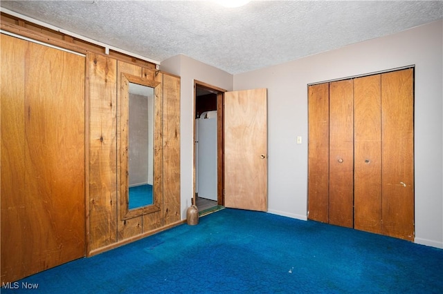 unfurnished bedroom with dark carpet, white fridge, and a textured ceiling