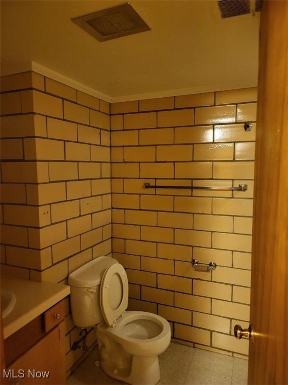 bathroom with tile patterned floors, toilet, crown molding, tile walls, and vanity