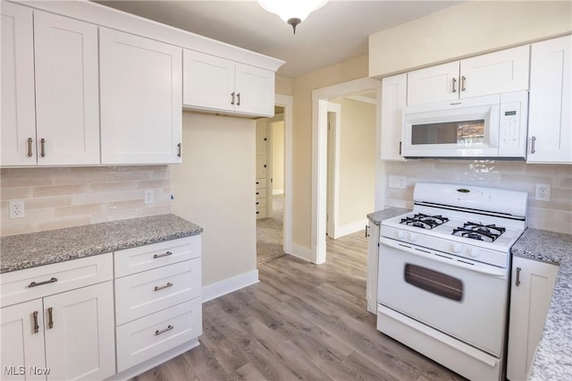 kitchen with white appliances, light stone countertops, light hardwood / wood-style floors, and white cabinets