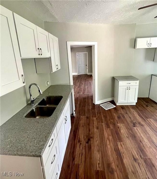 kitchen with sink, white cabinetry, dark stone countertops, dark hardwood / wood-style floors, and a textured ceiling