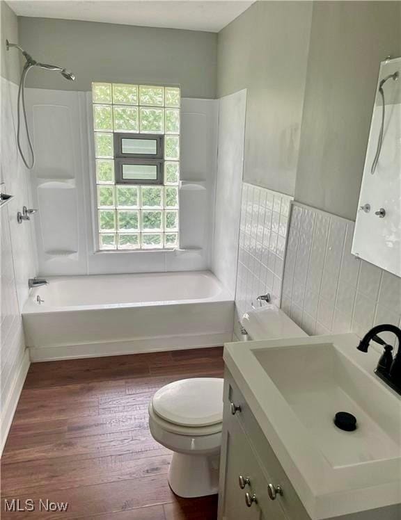 full bathroom with shower / tub combination, tile walls, hardwood / wood-style flooring, vanity, and toilet