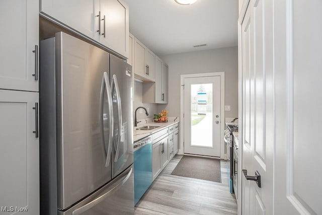 kitchen featuring appliances with stainless steel finishes, sink, white cabinets, and light hardwood / wood-style floors