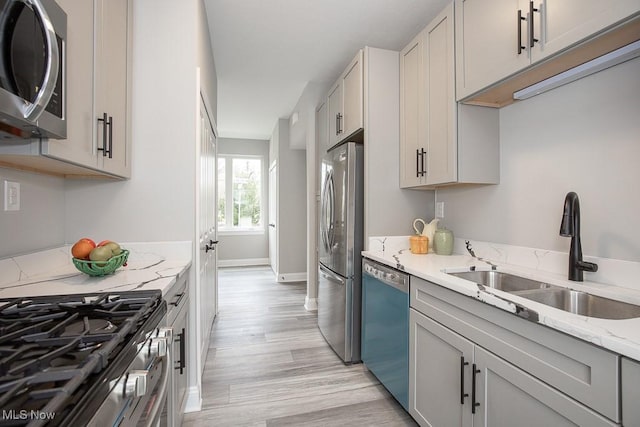 kitchen with sink, gray cabinetry, stainless steel appliances, light hardwood / wood-style floors, and light stone countertops