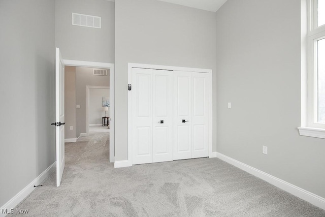 unfurnished bedroom with light colored carpet, a closet, and a high ceiling