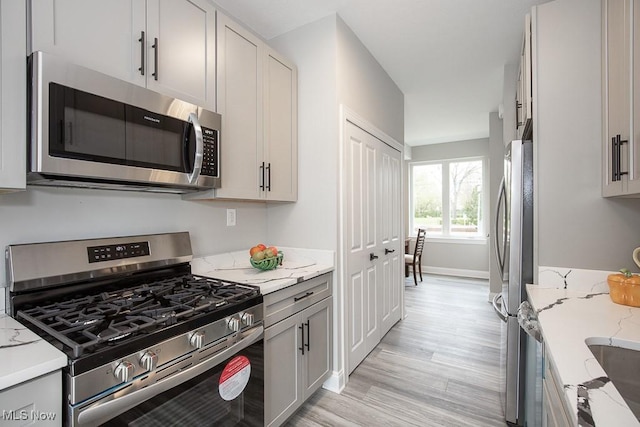 kitchen with stainless steel appliances, light stone counters, and light hardwood / wood-style floors