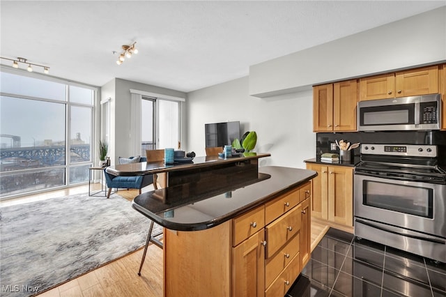 kitchen featuring a kitchen breakfast bar, a center island, stainless steel appliances, dark wood-type flooring, and track lighting