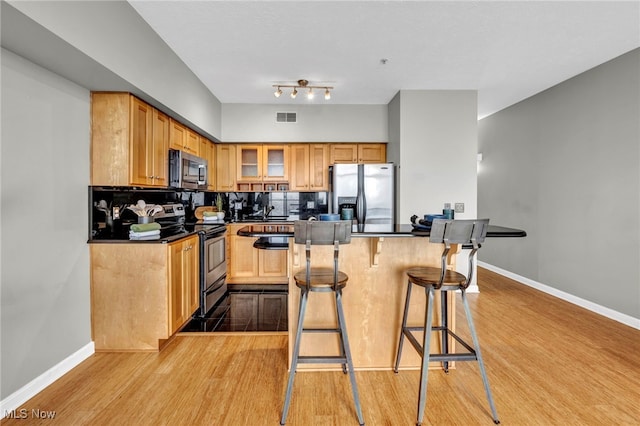 kitchen featuring backsplash, appliances with stainless steel finishes, a breakfast bar area, and light wood-type flooring