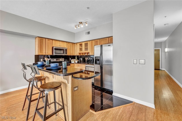 kitchen featuring a breakfast bar, a textured ceiling, dark hardwood / wood-style flooring, kitchen peninsula, and stainless steel appliances