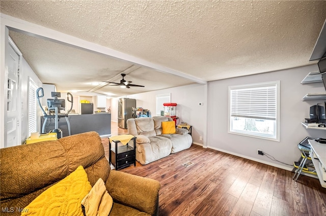 living room with ceiling fan, wood-type flooring, a textured ceiling, and vaulted ceiling with beams