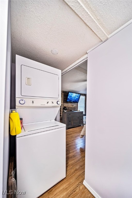 washroom featuring stacked washer / drying machine, light hardwood / wood-style floors, and a textured ceiling