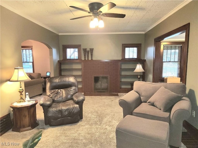 living room featuring ornamental molding, a brick fireplace, light colored carpet, and ceiling fan